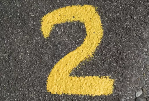 Das Bild zeigt die Zahl Zwei in gelb auf einer Straße.